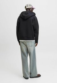 Sort hættetrøje, oversized pasform, kombineret med lyseblå loose fit jeans. Har en beige mesh baseball cap med en lyserød skygge.