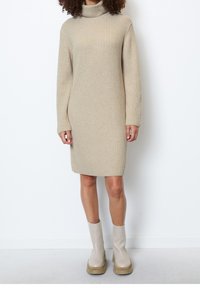 Robe beige côtelée à col roulé, manches longues, coupe droite et longueur genou. Portée avec des bottines à plateforme beige.