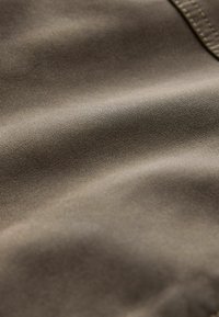 Close-up of soft, smooth brown fabric with subtle texture and visible stitching on the top right edge.