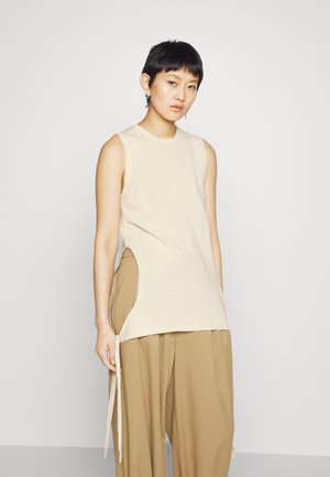 Top smanicato in maglia beige con scollo rotondo e dettagli con fessura laterale, abbinato a pantaloni larghi color marrone chiaro con rifiniture a cordoncino.