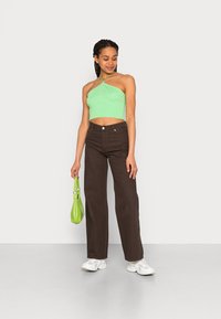 Top cropped verde claro com decote halter, combinado com calças de ganga castanhas de cintura alta, acessórios com uma pequena mala verde e ténis brancos.