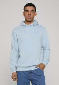 Sweat à capuche bleu clair en tissu doux avec capuche à cordon, manches longues, poignets côtelés et coupe décontractée, associé à un jean en denim bleu.