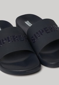 Infradito navy con logo lucido "SUPERDRY" sulla parte superiore, realizzati in materiale sintetico testurizzato, con design open-toe.