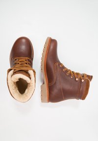 Botas de tobillo de cuero marrón con un interior forrado de forro polar, con cordones marrones, una parte superior texturizada y una suela resistente de color marrón claro.