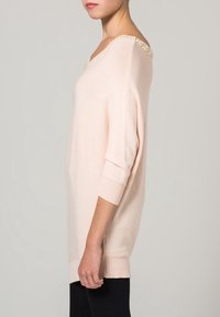 Maglione a maglia rosa chiaro con un collo ampio, decorato con dettagli in perle sulle spalle. Presenta maniche corte e una vestibilità comoda.