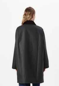 Casaco preto com silhueta ampla e mangas compridas, com gola de bombazina castanha. Textura suave, comprimento até ao joelho e detalhes mínimos.