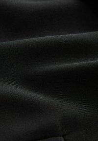 Tissu noir avec une surface texturée, présentant des plis et un léger éclat, indiquant un matériau lisse et durable.