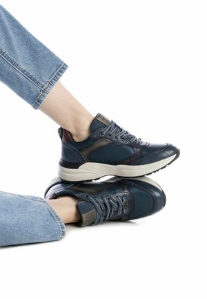 Zapatillas deportivas de color azul oscuro con cuero texturizado, diseño con cordones y acentos de cuero en contraste. Presentan una suela blanca gruesa.