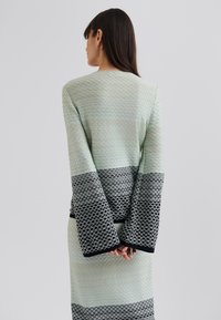 Haut à manches longues en tissu vert menthe texturé avec un motif en diamants, se transformant en une section inférieure rayée noire et grise.