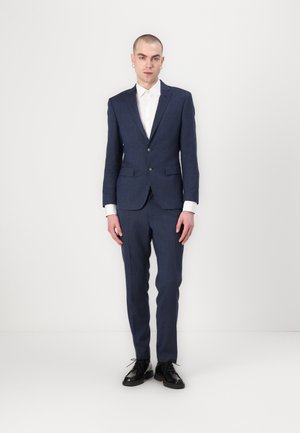 Navy blue suit with a tailored design, featuring a single-button jacket and flat-front pants, complemented by a white dress shirt and black shoes.
