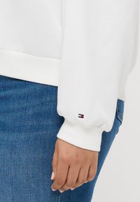 Hvid sweatshirt med ribbet manchet, med et lille logo i rød, hvid og blå på ærmet. Sammen med blå denim jeans.