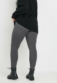 Leggings gris côtelés en tissu extensible, associés à des bottines noires à lacets. Les leggings présentent un design ajusté et une surface texturée.