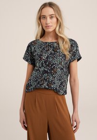 Top corto nero con un motivo astratto verde, marrone e bianco; vestibilità comoda con scollatura rotonda. Abbinato a pantaloni marroni a vita alta.