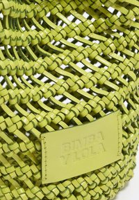 Wiklinowa zielona skórzana torba z geometrycznym wzorem, prostokątną naszywką z logo i gładką fakturą. Otwarty fason o ustrukturyzowanym kształcie.