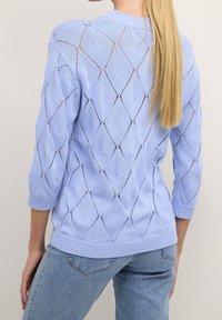 Jasnoniebieski sweter dzianinowy z wzorem w romby, o rękawach do łokcia i ściągaczu na dole. Posiada otwarte szycie w całej konstrukcji.