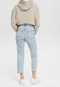 Haut à capuche beige avec une coupe courte, associé à un jean taille haute bleu clair et des baskets blanches à plateforme. La vue arrière met en avant les détails du design.