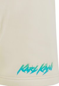 Bežinė trumpomis rankovėmis marškiniai su lygiu audinio tekstūru. Yra turkio spalvos ugnies stiliaus logotipas ant apvado, kontrastuojantis su neutraliu atspalviu.