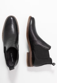 Černé kotníkové boty z texturované kůže s elastickými bočními panely a nízkým sloupkovým podpatkem. Na stélce mají decentní logo.