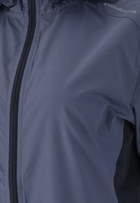 Giacca a vento leggera di colore blu navy con una texture liscia, zip a lunghezza completa e accenti neri; presenta il logo sulla spalla destra.