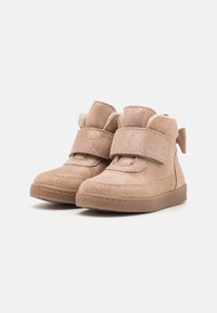 Tan suede ankle boots with a metallic finish, featuring a Velcro strap, rounded toe, and soft lining. Rubber sole with textured grip.