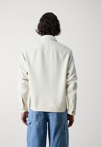 Witte gestructureerde blouse met een kraag en knoopmanchetten, gestyled met blauwe cargo broek. Het ontwerp heeft een relaxed fit en subtiele details.