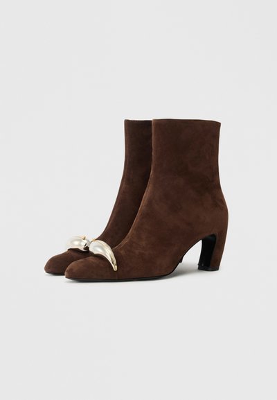 Brown suede ankle boots with a pointed toe and a curved metallic accent at the front. Features a moderate block heel. Smooth texture.