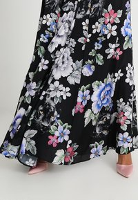 Robe longue noire à fleurs grandes avec des fleurs en rose, bleu et blanc, intégrant discrètement des visages de panthère dans le design.