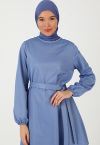 Langärmliges Kleid aus strukturiertem hellblauem Stoff, mit Rundhalsausschnitt, abnehmbarer Taillierung und einem fließenden Rock mit gerafften Akzenten.