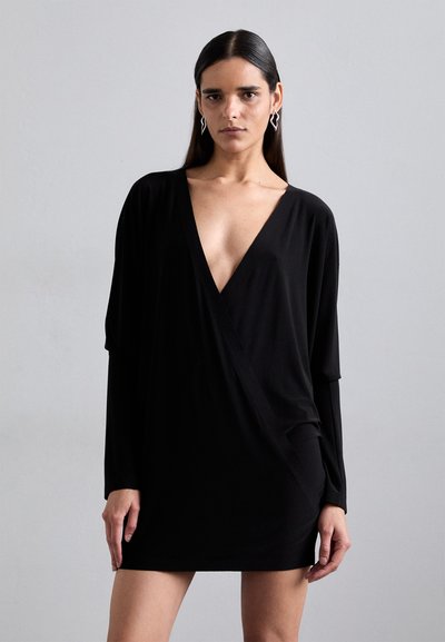 Robe portefeuille noire à manches longues, col en V profond, texture douce et détails froncés sur le côté, créant une silhouette élégante.