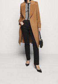 Brown wool coat with a wide collar over a black-and-white striped top, paired with black jeans and black pointed-toe heels. Black handbag.