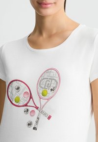 T-shirt blanc à manches courtes présentant un design brodé de deux raquettes de tennis avec des balles de tennis colorées et des accents scintillants.