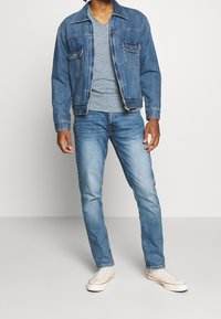 Jeansjacka med två bröstfickor, grå V-ringad t-shirt, ljusblå jeans och vita sneakers. Jackan har en klassisk passform och en blekt struktur.