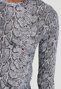Langarmshirt mit einem schwarz-weißen Schlangenledermuster. Glatte Textur mit tailliertem Schnitt und rundem Ausschnitt.