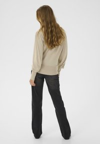 Maglione beige lavorato a maglia con una vita aderente, abbinato a jeans neri a zampa d'elefante. Il maglione presenta maniche lunghe a sbuffo e una texture liscia.
