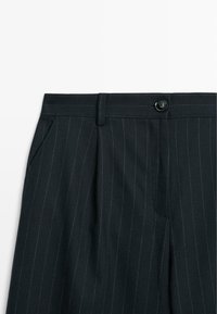 Sorte stribede bukser med et elegant design, der har en frontknap, skræddersyede gennemskæringer og sidelommer i struktureret stof.