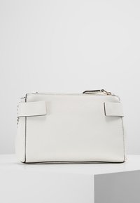 Clutch bag in pelle bianca texturizzata con zipper superiore e dettagli della tracolla, posizionata su una superficie bianca contro uno sfondo grigio chiaro.