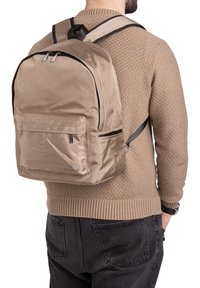 Sac à dos en nylon beige avec des bretelles réglables, deux compartiments zippés et une poche avant ; texture lisse et élégante, design minimaliste.