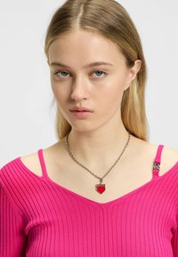 Rosa ribbat topp med off-shoulder-design, med metallhardware-accenter. Kedjesmycke med röd hjärtformad berlock och "Hugo"-gravyr.