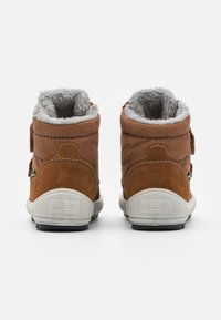Braune Wildleder-Stiefeletten mit Kunstfellfutter, Klettverschluss und Gummisohle. Mit weißer Außensohle mit strukturiertem Muster und Markenlogo.