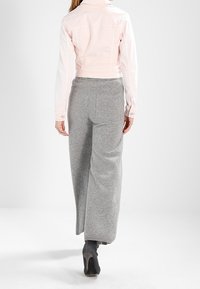 Ljust rosa kort denimjacka, grå vida stickade byxor och svarta högklackade skor sedda bakifrån.