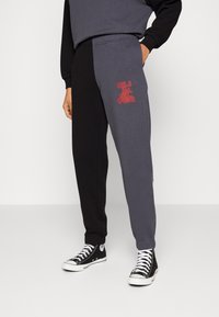 Persona vestida con pantalones de chándal bicolor en negro y gris, con el logo rojo de Quiksilver en la pierna gris y zapatillas de deporte negras de caña alta.
