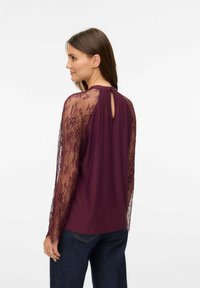 Blusa bordeaux con maniche in pizzo trasparente e dettaglio a chiave sul retro, caratterizzata da un design fluido e una texture liscia.