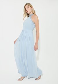 Lungo vestito blu chiaro con gonna plissettata, collo all'americana e dettagli in argento. Caratterizzato da un tessuto fluido e un corpetto aderente.