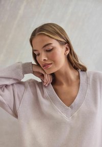 Jasnoszara, oversize'owa bluza z dekoltem w kształcie litery V, ribbowym wykończeniem dekoltu oraz teksturowanym materiałem. Posiada luźne rękawy i miękkie wykończenie.