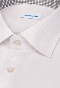 Chemise beige clair en tissu texturé, avec un col classique, une fermeture à boutons et un col intérieur contrastant à motif.