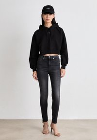 Black cropped hoodie with drawstrings, paired with high-waisted dark jeans and beige heeled sandals. Black cap completes the outfit.
