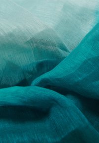 Tissu turquoise transparent avec un tissage léger et texturé, affichant de douces plis et des variations subtiles de couleur et de lumière.