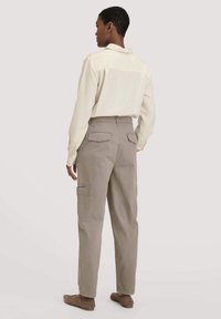 Beige cargobroek met zijzakken, gecombineerd met een lichtgekleurde shirt. De broek heeft een relaxte pasvorm en een gestructureerde tailleband.