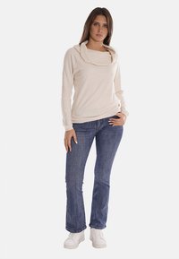 Maglione beige con collo a cowl, in materiale morbido, maniche lunghe, abbinato a jeans a zampa d'elefante blu e sneakers bianche con plateau. Design semplice e privo di ornamenti.
