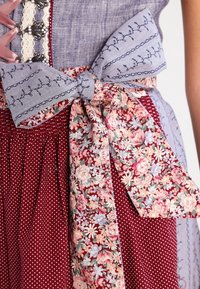 Robe en tissu avec une jupe rouge à pois, un tissu à motif floral, des accents bleu lavande et un nœud à la taille avec des coutures décoratives.